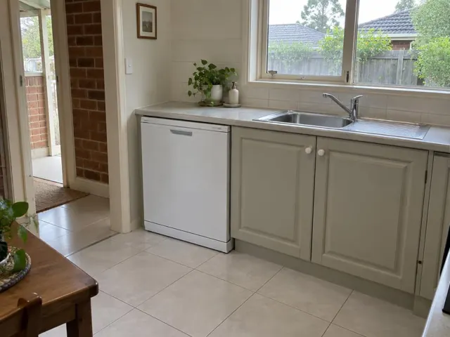 White dishwasher under a kitchen benchtop beside a sink with tiled splashback in Awaba