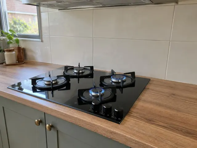 Black gas cooktop set into a timber-look kitchen benchtop with tiled splashback in Toronto