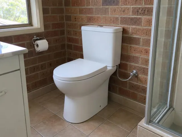 White toilet beside a vanity and shower screen in a tiled brick bathroom in Kilaben Bay